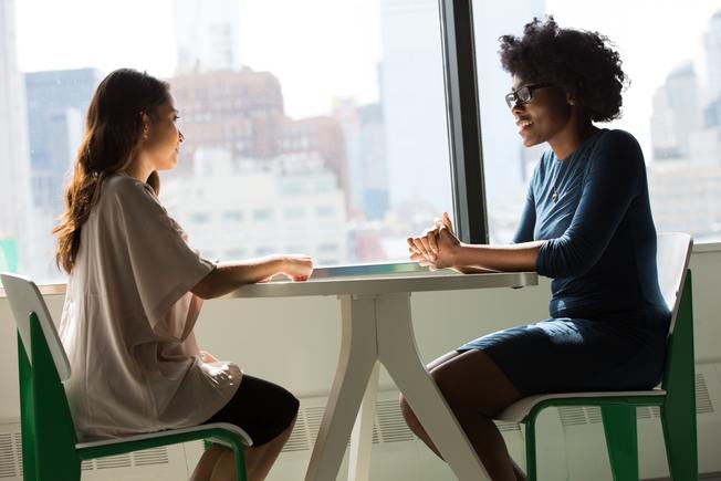 Desktop two women sitting on chairs beside window 1181719