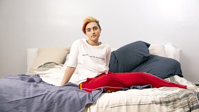 Desktop a transmasculine gendernonconforming person sitting on a bed